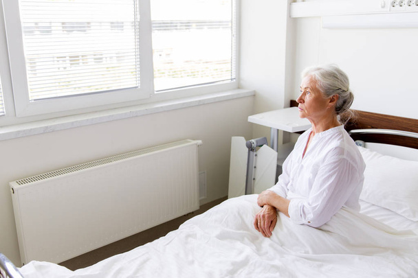 θλιβερή ανώτερων γυναίκα που κάθεται στο κρεβάτι στο νοσοκομείο ward - Φωτογραφία, εικόνα