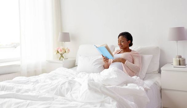 happy pregnant african woman reading book at home - Фото, изображение