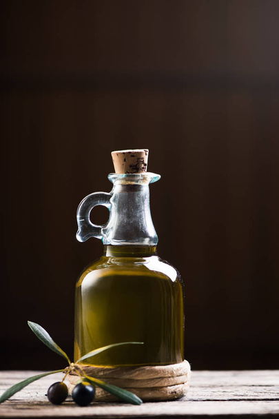 Botella de aceite de oliva y olivos sobre mesa de madera
 - Foto, Imagen
