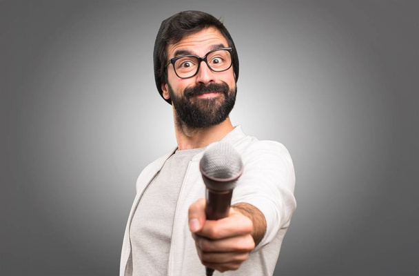 Hipster man zingen met microfoon op grijze achtergrond - Foto, afbeelding