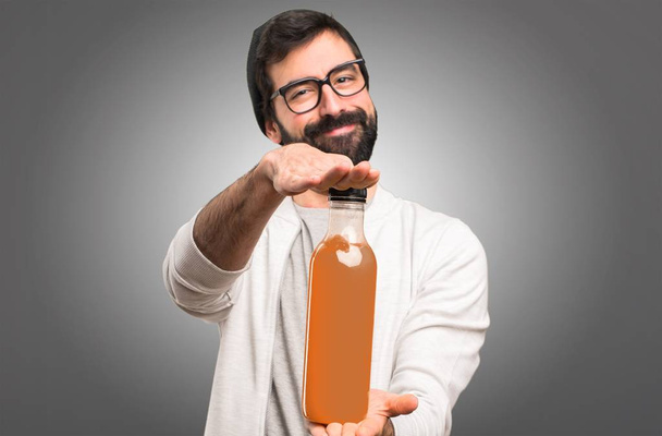 Feliz hombre Hipster sosteniendo un jugo de naranja sobre fondo gris
 - Foto, Imagen
