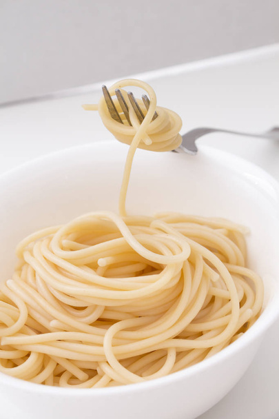 白いボール、フォーク、白い背景の上にプレーンの調理スパゲッティ パスタ. - 写真・画像