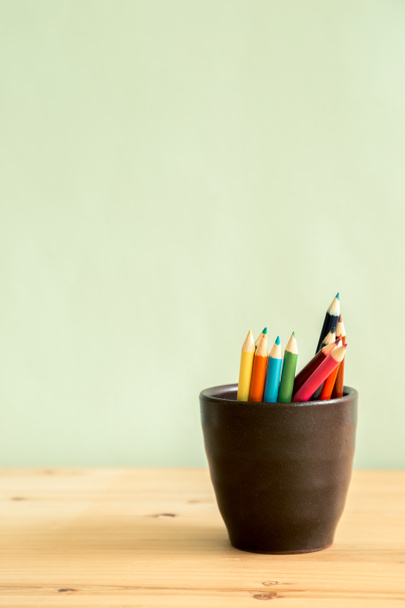 Кольорові олівці в коричневій керамічній чашці на дерев'яному столі
 - Фото, зображення