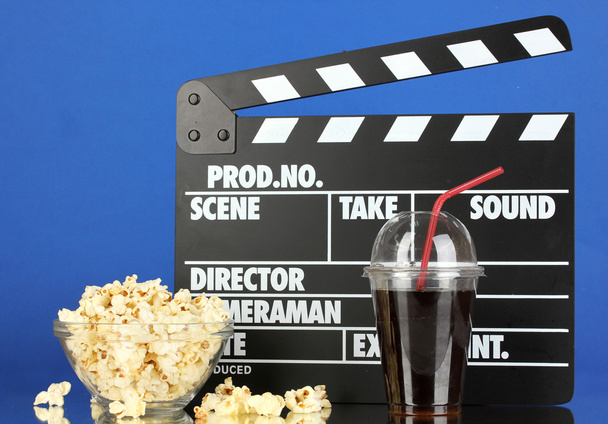 Movie clapperboard, cola and popcorn on blue background - Photo, Image