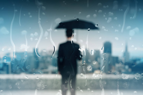 Back view of blurry young businessman with umbrella on roof top with rain drops. Safety concept  - Photo, image