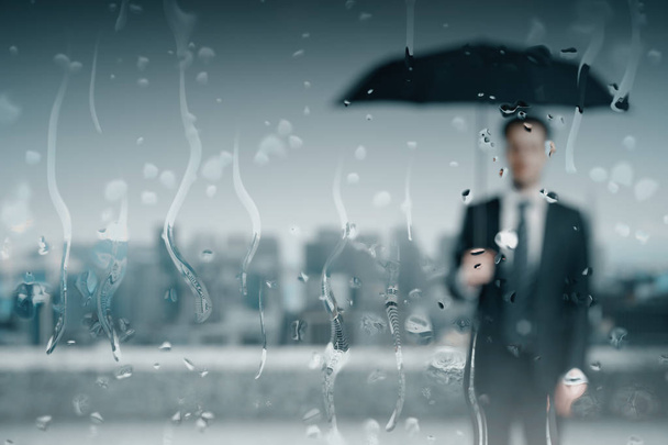 Back view of blurry young businessman with umbrella on roof top with rain drops. Protection concept  - Foto, Bild