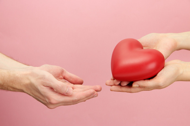 Red heart in woman and man hands, on pink background - Photo, Image