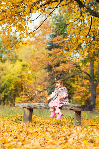 Happy little baby girl sitting on a bench laughing and playing with leaves. In nature, walk in the open air - Fotoğraf, Görsel