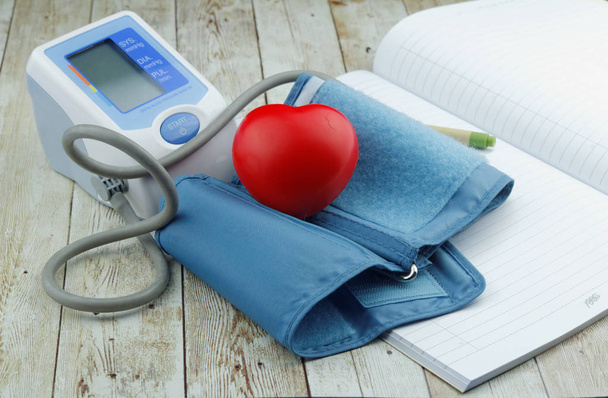 Blutdruckmessgerät, Herzform-Symbol und leeres Notizbuch auf Holzgrund. - Foto, Bild