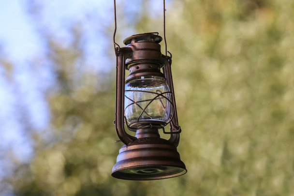 Vecchia lampada ad olio arrugginita appesa a un gancio di metallo da un palo di legno all'aperto
 - Foto, immagini