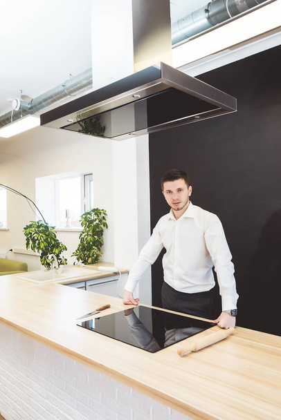 young stylish man in a white shirt is standing in a modern kitchen - Фото, изображение
