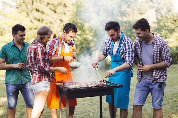 Happy friends grilling meat and enjoying barbecue party outdoors - Foto, Imagem