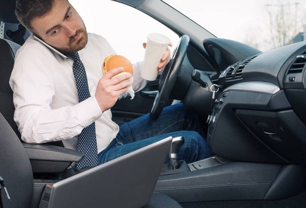 Hombre comiendo comida de engorde y trabajando sentado en coche
 - Foto, imagen