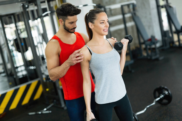 Young adult woman working out in gym doing biceps with trainer - Photo, Image