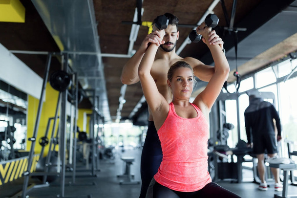 Beautiful girl doing exercises with personal trainer in gym - Foto, Imagem