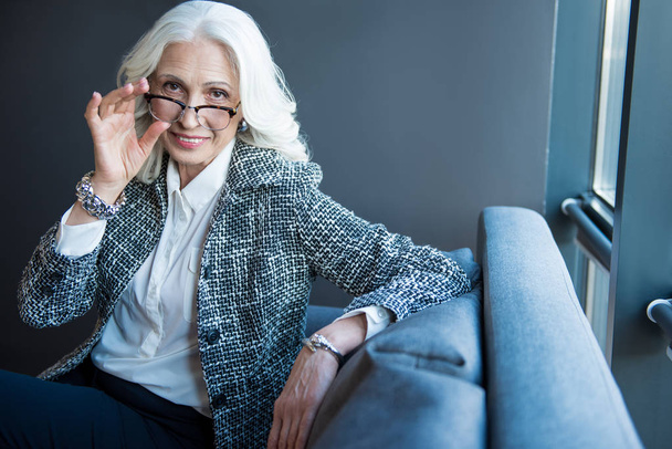 Positive senior elegant businesswoman is sitting on sofa - Photo, image
