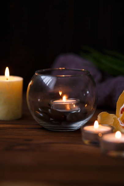Una vela en un jarrón de vidrio, decoración y varios elementos interesantes sobre un fondo de madera oscura. Velas encendidas. Set para spa y masaje
. - Foto, imagen