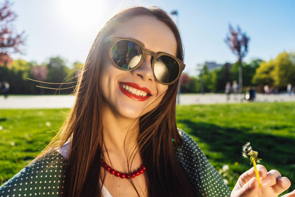 Щасливі усміхнені смішні обличчя дівчина дме кульбабу, літні сонцезахисні окуляри, захід сонця
 - Фото, зображення
