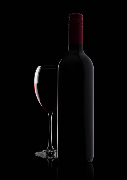 Glass of red wine with bottle with shape on black - Фото, зображення