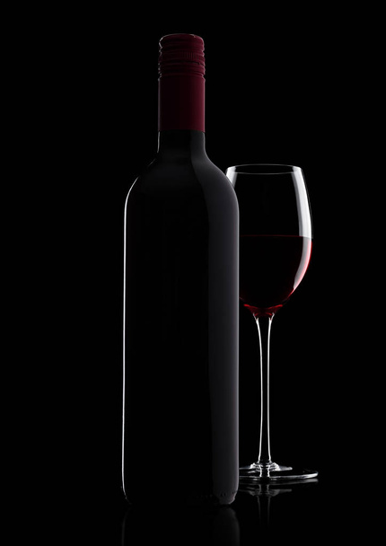 Glass of red wine with bottle with shape on black - Foto, imagen