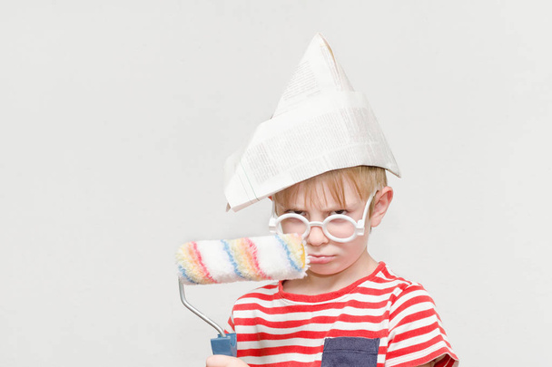 Αγόρι σε ένα καπέλο χαρτί παίζει σε ένα ζωγράφο. Πορτρέτο. Ρολό για βάψιμο - Φωτογραφία, εικόνα