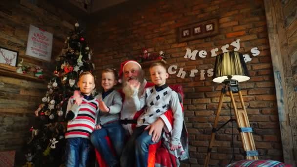 3 人の男の子の兄弟がサンタ クロースに願いし、飾られたお祝い部屋の肘掛け椅子に座って、今後のクリスマス休暇のお祝いの言葉とあいさつを送信 - 映像、動画