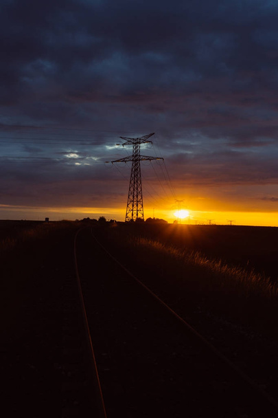 High voltage power lines and transmission towers at sunset. Poles and overhead power lines silhouettes in the dusk. Electricity generation and distribution. Electric power industry and nature concept - Photo, Image