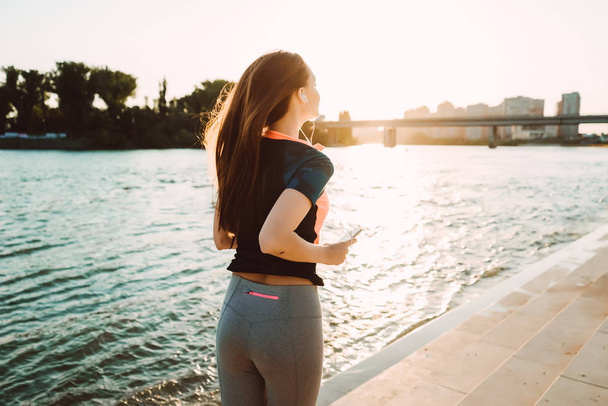 long-haired girl runs by the river at sunset, listens to music on headphones - Foto, Imagem
