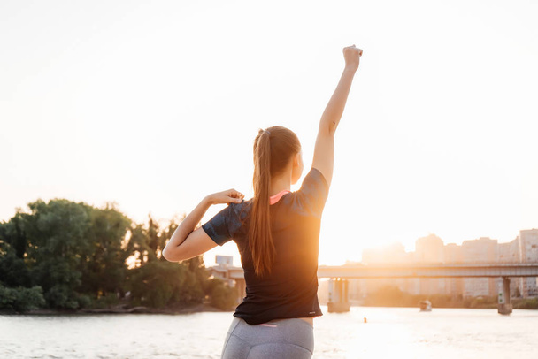 tenké sportovní dívka fyzičce u řeky při západu slunce, poslechu hudby ve sluchátkách - Fotografie, Obrázek