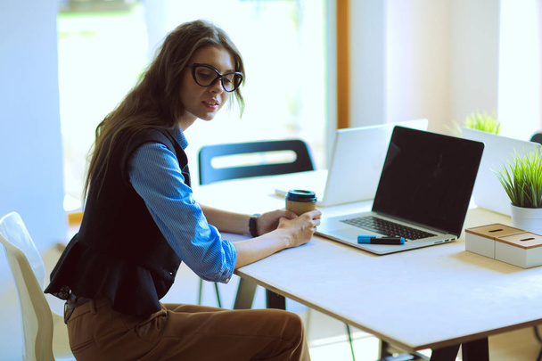 Egy fiatal nő ül az irodai asztalnál laptoppal. Fiatal nő. Laptop - Fotó, kép
