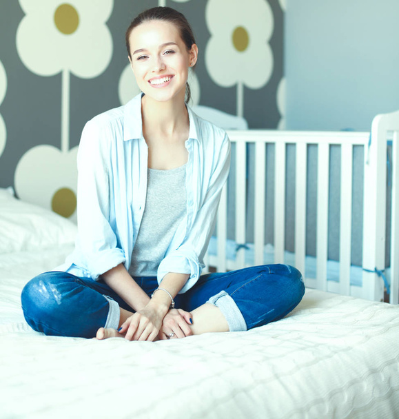 Young woman sitting on the bed near childrens cot - Fotoğraf, Görsel