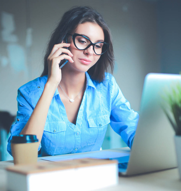 Beautiful young business woman sitting at office desk and talking on cell phone - Foto, imagen