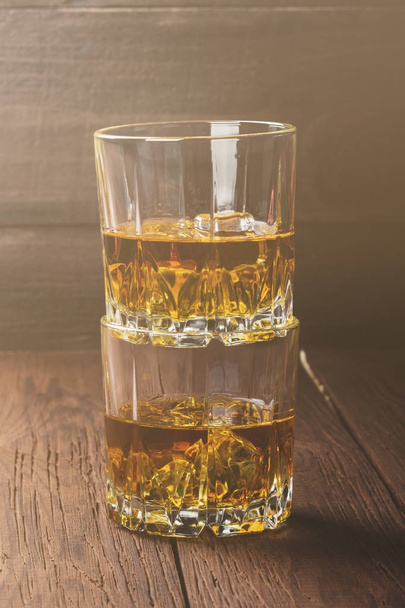Whisky with ice in two glasses on a wooden background. Toned - Fotografie, Obrázek