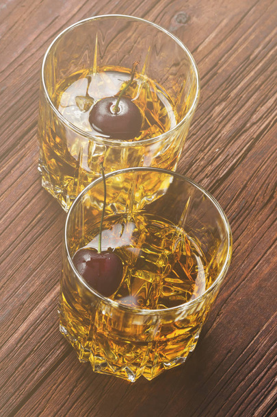Cocktail from whisky with cherry in two glasses on a wooden back - Fotó, kép