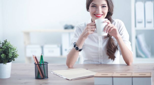 Young businesswoman sitting on the desk with cup in office - Zdjęcie, obraz