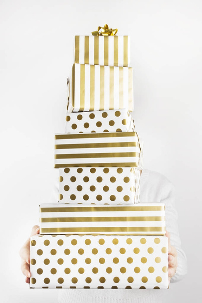 Woman holding group of gifts in white and gold paper on a gray b - Foto, Imagen