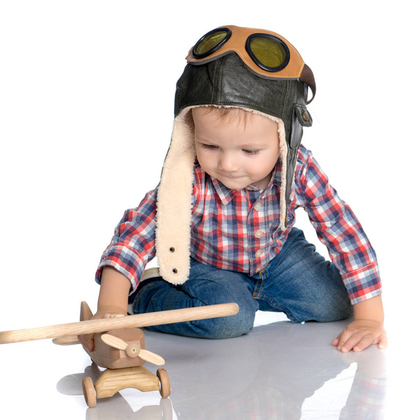 A little boy in a pilots cap and a wooden plane in his hand - Foto, immagini