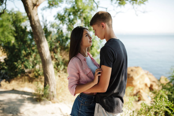 Portrait of young beautiful couple standing and dreamily looking on each other while spending time together with sea view on background - Photo, Image