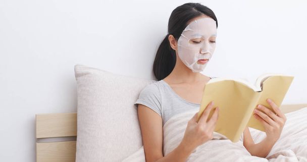 Женщина в маске для лица и читает книгу на кровати
  - Фото, изображение