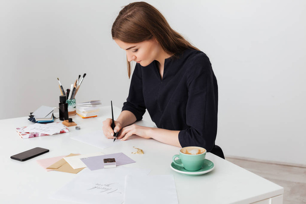 Muotokuva nuori kaunis nainen istuu valkoisella pöydällä kuppi kahvia ja kirjallisesti paperilla eristetty
 - Valokuva, kuva