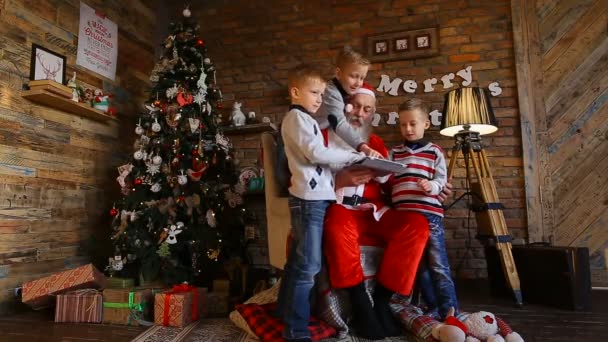 Fidgety meninos juntos passar o seu tempo de lazer e jogar em tablet junto com o Papai Noel em sala festiva com bela árvore de Natal
 - Filmagem, Vídeo