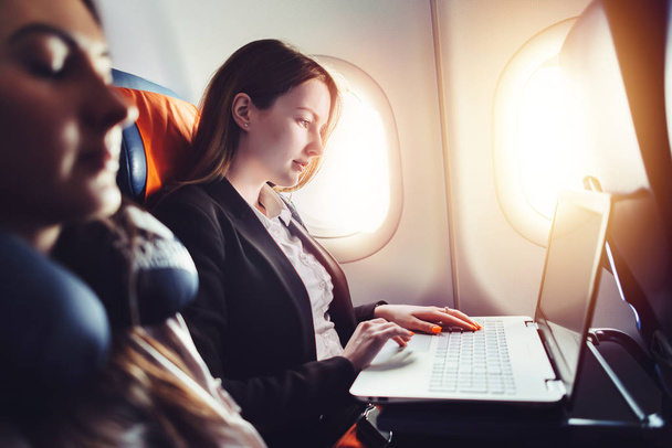 Женщина-предприниматель, работающая на ноутбуке, сидит у окна в самолете
 - Фото, изображение