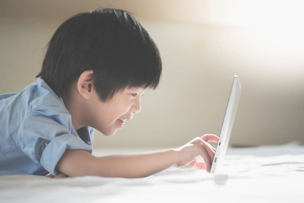 Aranyos ázsiai fiú feküdt az ágyban, és használ a laptop a fehér ágy - Fotó, kép