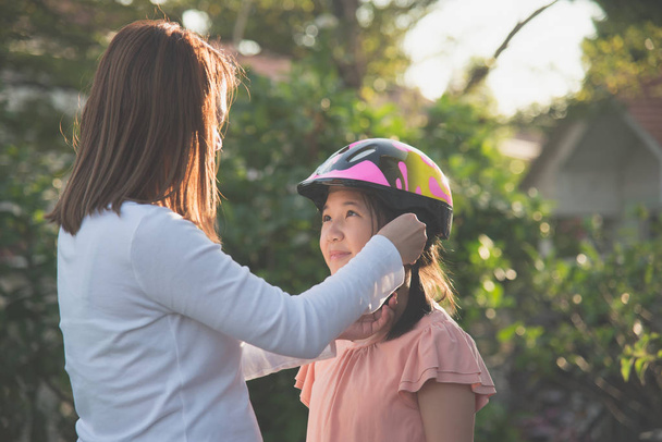 アジアの母は彼女の娘に自転車のヘルメットを着ています。 - 写真・画像