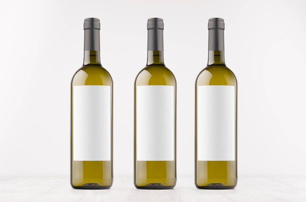 Three green wine bottles with blank white labels on white wooden board, mock up.  - Photo, Image