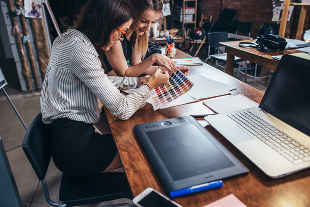 Deux architectes féminines travaillant ensemble en utilisant des échantillons de couleur assis au bureau avec ordinateur portable, tablette graphique dans le studio de design
 - Photo, image