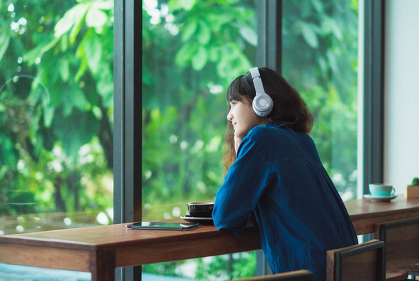Happy asian casual woman listening music with headphones near wi - Zdjęcie, obraz