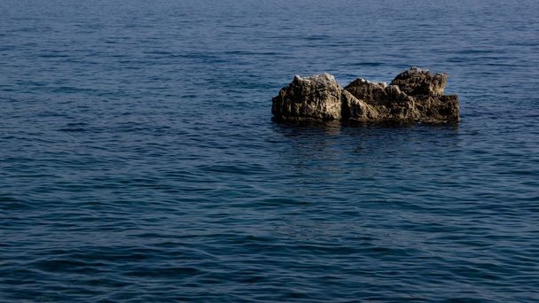 Κλείνω πάνω θέα ένα γκρι βράχο που περιβάλλεται από τη γαλάζια θάλασσα.  - Φωτογραφία, εικόνα
