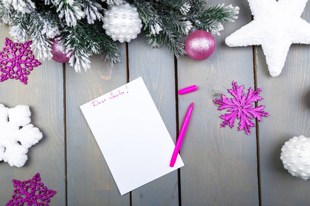das Blatt Papier, rosa Bleistifte und Weihnachtsdekorationen auf einem hölzernen Hintergrund. Konzept von Neujahr und Weihnachten. Ansicht von oben. flache Lage - Foto, Bild