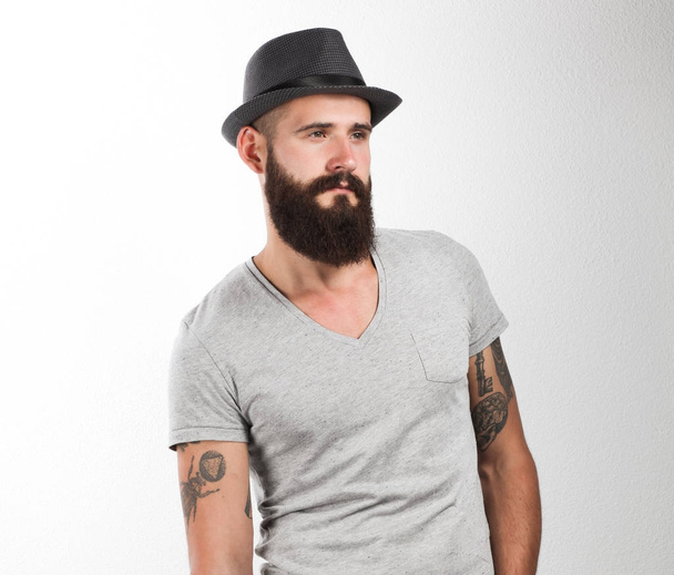 Portrait of handsome bearded man in hat standing with bad, isolated on white background - Foto, Imagen